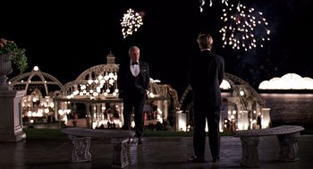Two men in tuxedos standing in front of fireworks at night