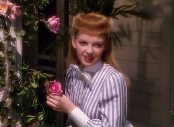Movie still from “Meet Me in St. Louis” (1944), directed by Vincente Minnelli – A young woman holding a pink rose in front of a bush; Medium shot, High angle