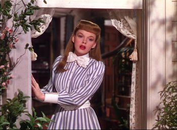 Movie still from “Meet Me in St. Louis” (1944), directed by Vincente Minnelli – A woman in a striped dress standing in front of a window; Medium shot, Low angle