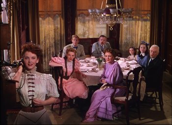 Movie still from “Meet Me in St. Louis” (1944), directed by Vincente Minnelli – A group of people sitting around a table with plates of food on it; Wide shot, High angle