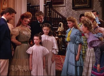 Movie still from “Meet Me in St. Louis” (1944), directed by Vincente Minnelli – A group of people standing around each other in front of a staircase; Medium shot, High angle