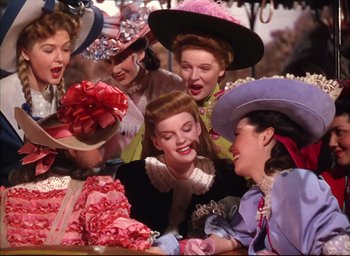 Movie still from “Meet Me in St. Louis” (1944), directed by Vincente Minnelli – A group of women wearing hats and holding bows; Medium shot, Low angle