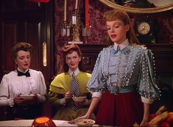 Movie still from “Meet Me in St. Louis” (1944), directed by Vincente Minnelli – A group of women standing around a table with food on top of it; Medium shot, Low angle