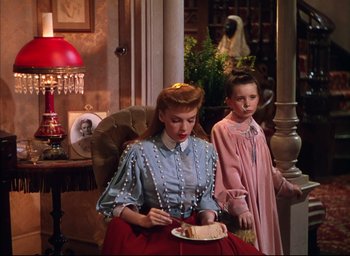 Movie still from “Meet Me in St. Louis” (1944), directed by Vincente Minnelli – A woman sitting next to a young girl holding a plate of food; Medium shot, High angle