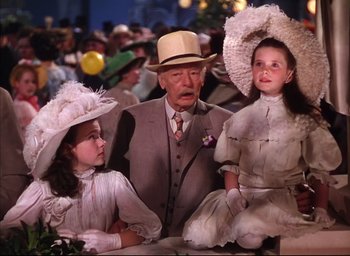 Movie still from “Meet Me in St. Louis” (1944), directed by Vincente Minnelli – A man and two little girls wearing hats; Medium shot, Low angle