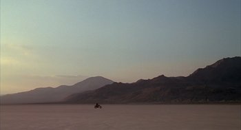 Movie still from “Melvin and Howard” (1980), directed by Jonathan Demme – A person riding a motorcycle in the middle of the desert; Extreme Wide shot, Low angle