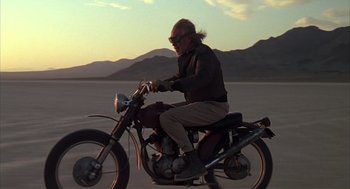 Movie still from “Melvin and Howard” (1980), directed by Jonathan Demme – An older man riding a motorcycle on the beach at sunset; Wide shot, Low angle