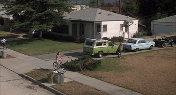 Movie still from “Melvin and Howard” (1980), directed by Jonathan Demme – A man riding a bike down a street next to a green truck; Extreme Wide shot, High angle