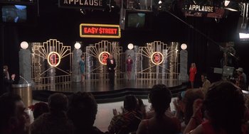 Movie still from “Melvin and Howard” (1980), directed by Jonathan Demme – A group of people sitting in front of a stage; Wide shot, Over the shoulder angle