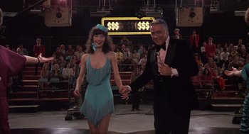 Movie still from “Melvin and Howard” (1980), directed by Jonathan Demme – A man and a woman holding hands in front of an audience; Medium shot, Low angle