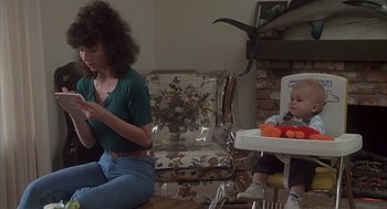Movie still from “Melvin and Howard” (1980), directed by Jonathan Demme – A woman sitting on the floor next to a baby in a high chair; Medium shot, Low angle