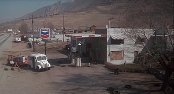 Movie still from “Melvin and Howard” (1980), directed by Jonathan Demme – An old gas station with a car parked on the side of the road; Extreme Wide shot, High angle