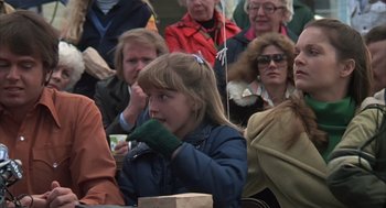 Movie still from “Melvin and Howard” (1980), directed by Jonathan Demme – A little girl wearing a green glove while sitting in front of a group of people; Medium shot, Over the shoulder angle