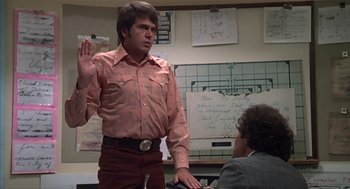 Movie still from “Melvin and Howard” (1980), directed by Jonathan Demme – A man in an orange shirt is being sworn in by another man; Medium shot, Over the shoulder angle