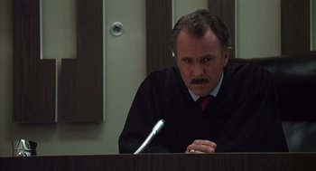 Movie still from “Melvin and Howard” (1980), directed by Jonathan Demme – A man sitting at a table in front of a microphone in a courtroom; Close Up shot, Low angle