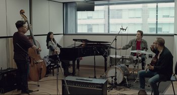A group of people playing musical instruments in front of a large window