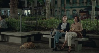 Two people sitting on a bench with a dog laying on the ground