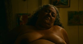 Movie still from “Memory House” (2020), directed by João Paulo Miranda Maria – An older woman with curly hair and a large breast; Close Up shot, Low angle