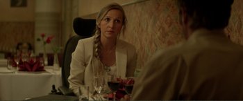 Movie still from “Men & Chicken” (2015), directed by Anders Thomas Jensen – A woman sitting at a table with a glass of wine; Medium shot, Over the shoulder angle