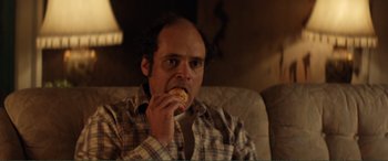 Movie still from “Men & Chicken” (2015), directed by Anders Thomas Jensen – A man sitting on a couch eating a donut; Close Up shot, Over the shoulder angle