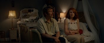 Movie still from “Men & Chicken” (2015), directed by Anders Thomas Jensen – A man and a woman sitting on a couch in front of a lamp; Medium shot, Over the shoulder angle