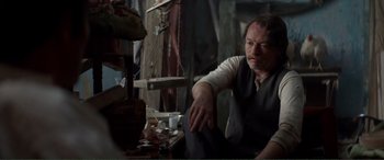 Movie still from “Men & Chicken” (2015), directed by Anders Thomas Jensen – A man sitting on a chair in a room; Medium shot, Over the shoulder angle