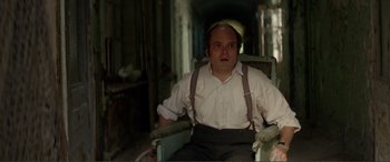 Movie still from “Men & Chicken” (2015), directed by Anders Thomas Jensen – A man sitting in a chair wearing suspenders and a hat; Medium shot, High angle