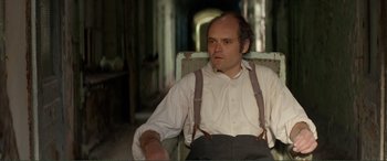 Movie still from “Men & Chicken” (2015), directed by Anders Thomas Jensen – A man sitting in a chair wearing suspenders; Medium shot, High angle