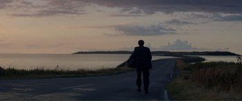 Movie still from “Men & Chicken” (2015), directed by Anders Thomas Jensen – A man walking down a road near a body of water; Extreme Wide shot, Over the shoulder angle