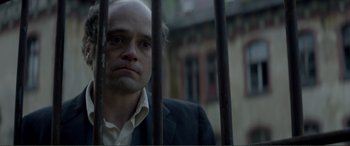 Movie still from “Men & Chicken” (2015), directed by Anders Thomas Jensen – A man in a suit behind a metal fence; Close Up shot, Over the shoulder angle