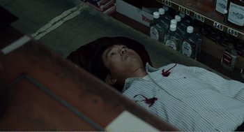 Movie still from “Menace II Society” (1993), directed by Albert Hughes – A man is laying in a bed with blood on his shirt; Medium shot, Overhead angle