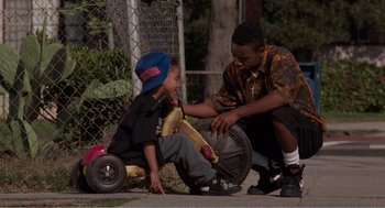 Movie still from “Menace II Society” (1993), directed by Albert Hughes – A man helping a boy with a banana peel; Medium shot, Over the shoulder angle