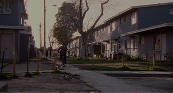 Movie still from “Menace II Society” (1993), directed by Albert Hughes – A person riding a bike down a street near some buildings; Extreme Wide shot, High angle