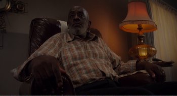 Movie still from “Menace II Society” (1993), directed by Albert Hughes – An older man sitting in a chair in front of a lamp; Medium shot, Low angle