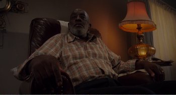 Movie still from “Menace II Society” (1993), directed by Albert Hughes – An older man sitting in a chair in a living room; Medium shot, Low angle