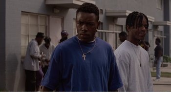 Movie still from “Menace II Society” (1993), directed by Albert Hughes – A young man wearing a blue shirt with a cross on it; Close Up shot, Low angle