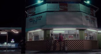 Movie still from “Menace II Society” (1993), directed by Albert Hughes – Three people standing outside of a restaurant at night; Extreme Wide shot, High angle