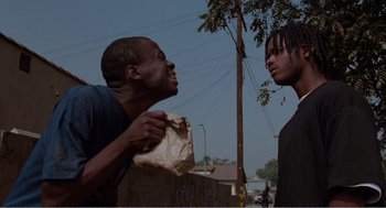 Movie still from “Menace II Society” (1993), directed by Albert Hughes – Two young men standing next to each other on a street; Medium shot, Low angle