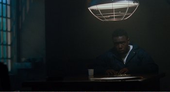 Movie still from “Menace II Society” (1993), directed by Albert Hughes – A man sitting at a table in front of a lamp; Medium shot, High angle