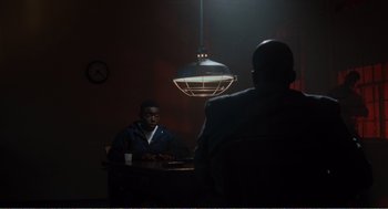 Movie still from “Menace II Society” (1993), directed by Albert Hughes – A man sitting at a table in front of another man; Medium shot, Over the shoulder angle