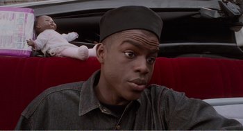 Movie still from “Menace II Society” (1993), directed by Albert Hughes – A young man wearing a black hat sitting on a red couch; Close Up shot, High angle
