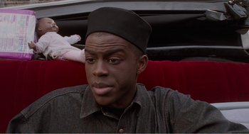 Movie still from “Menace II Society” (1993), directed by Albert Hughes – A young man wearing a black hat sitting on a red couch; Close Up shot, Over the shoulder angle