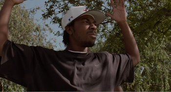 Movie still from “Menace II Society” (1993), directed by Albert Hughes – A person wearing a hat near a tree; Close Up shot, Low angle
