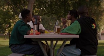 Movie still from “Menace II Society” (1993), directed by Albert Hughes – A group of people sitting at a picnic table; Medium shot, High angle