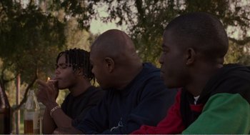 Movie still from “Menace II Society” (1993), directed by Albert Hughes – A group of young men sitting next to each other on the ground; Medium shot, Low angle