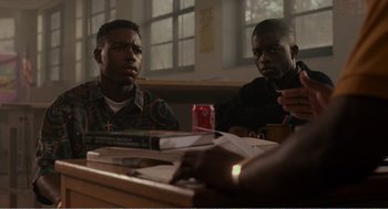 Movie still from “Menace II Society” (1993), directed by Albert Hughes – A couple of men sitting at a wooden table; Medium shot, Over the shoulder angle