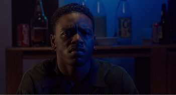 Movie still from “Menace II Society” (1993), directed by Albert Hughes – A man sitting at a table in front of a bottle; Close Up shot, Low angle