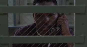 Movie still from “Menace II Society” (1993), directed by Albert Hughes – A man talking on a cell phone behind bars; Close Up shot, Low angle