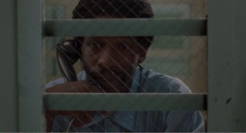 Movie still from “Menace II Society” (1993), directed by Albert Hughes – A man sitting in front of a fence talking on a phone; Close Up shot, High angle
