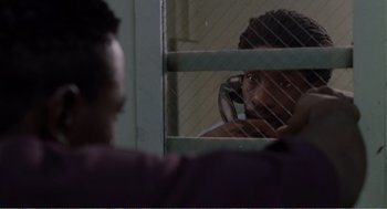 Movie still from “Menace II Society” (1993), directed by Albert Hughes – A man looking out of a window at another man through a fence; Close Up shot, Over the shoulder angle